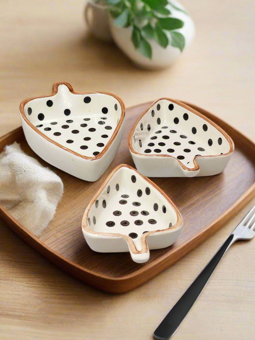 Three ceramic dragon fruit-shaped bowls on a wooden tray with a plant in the background.