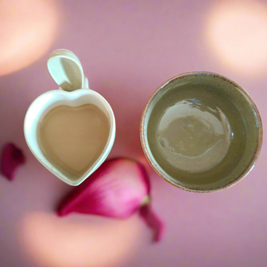 A set of ceramic breakfastware consisting of a bowl and a mug, with the bowl displayed upside down next to a spoon, all against a pink background.