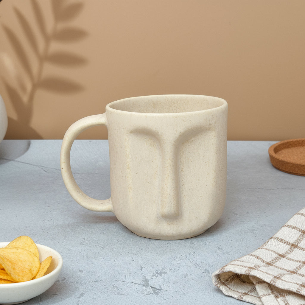 Beige ceramic mug with face design on a gray surface