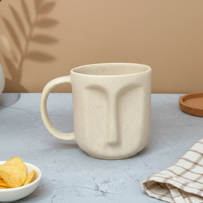 Beige ceramic mug with face design on a gray surface