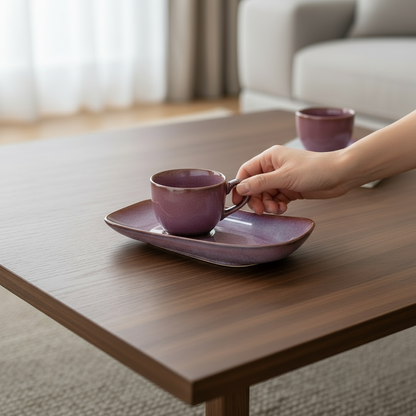 Hand placing a purple ceramic cup on a matching saucer on a wooden table.