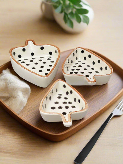 Three ceramic dragon fruit-shaped bowls on a wooden tray with a plant in the background.