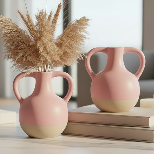 Two pink vases with beige bases on a surface with books and a candle.